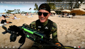 YouTuber Jake Koehler stands on a beach holding a waterproof metal detector.